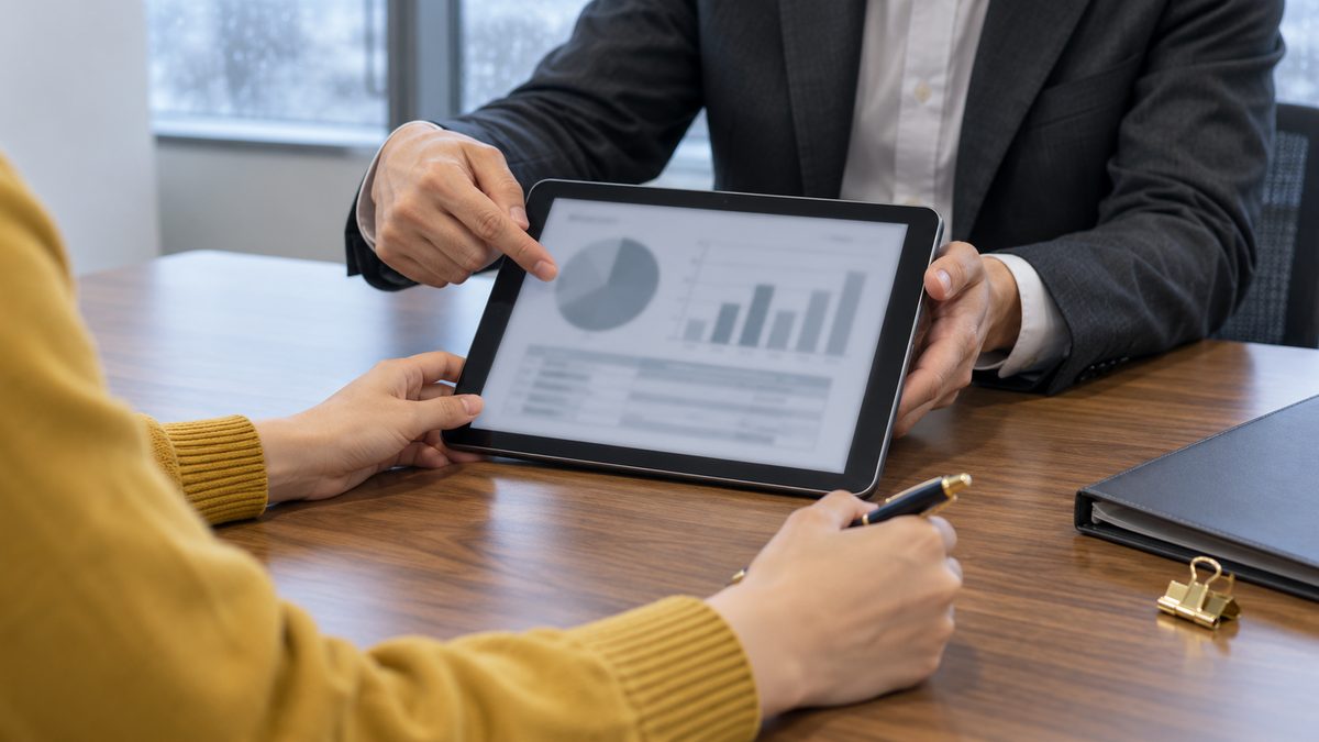タブレットのグラフを指して説明する担当者とペンを持つ担当者の手元