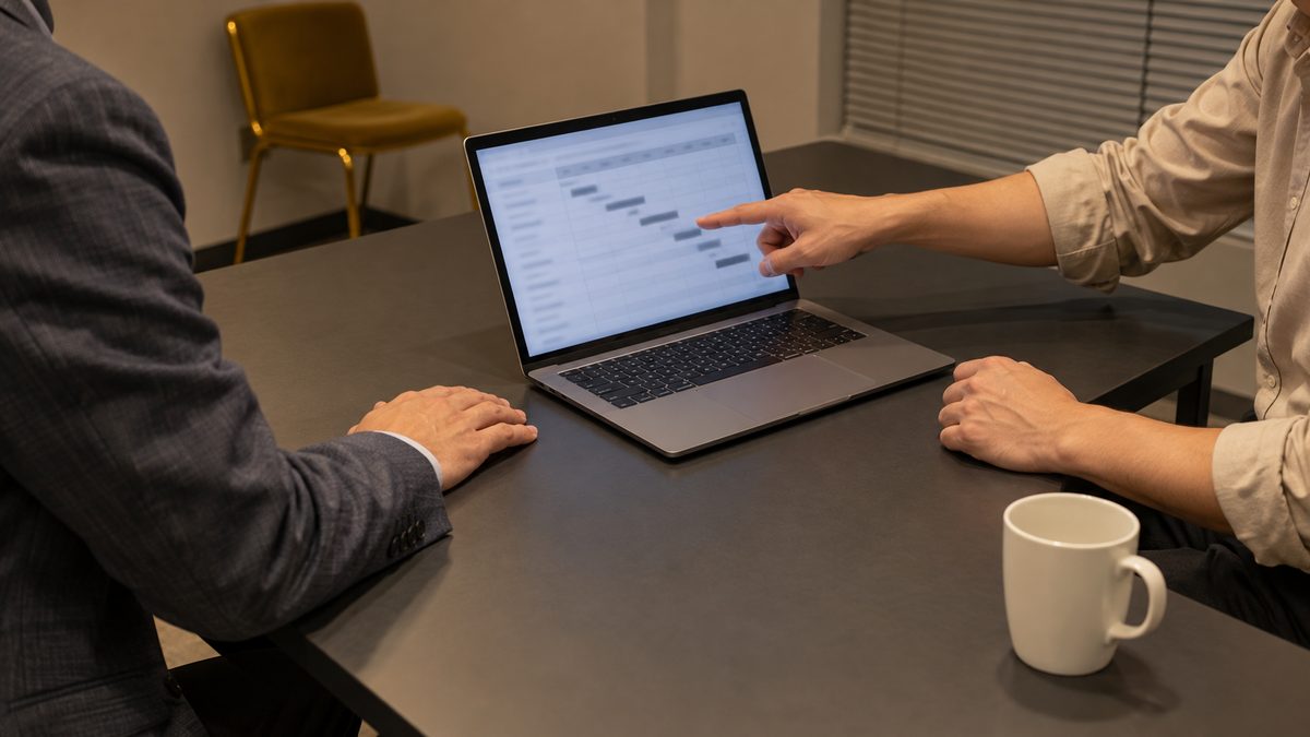 打ち合わせ机でノートPCの予定表を指して確かめる担当者と技術者の手元