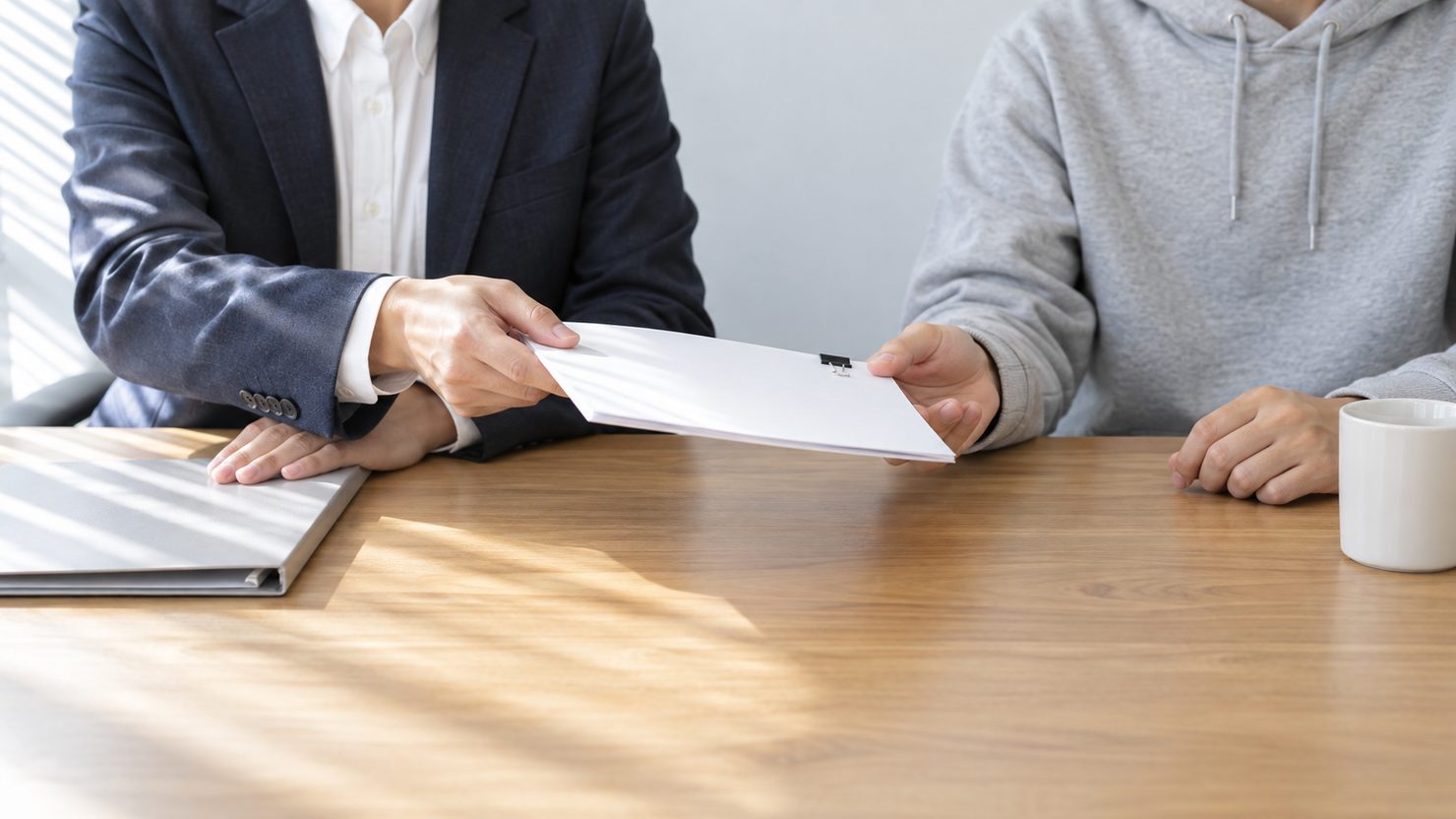 人事の担当者が面接官を務めるエンジニアにクリップ留めの面接の手引きを手渡す会議室の手元