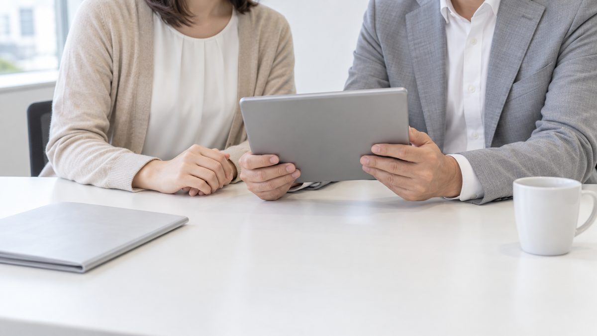会議室の白い机で人事担当者と開発マネージャーが並んで座り1台のタブレットを一緒に見ている