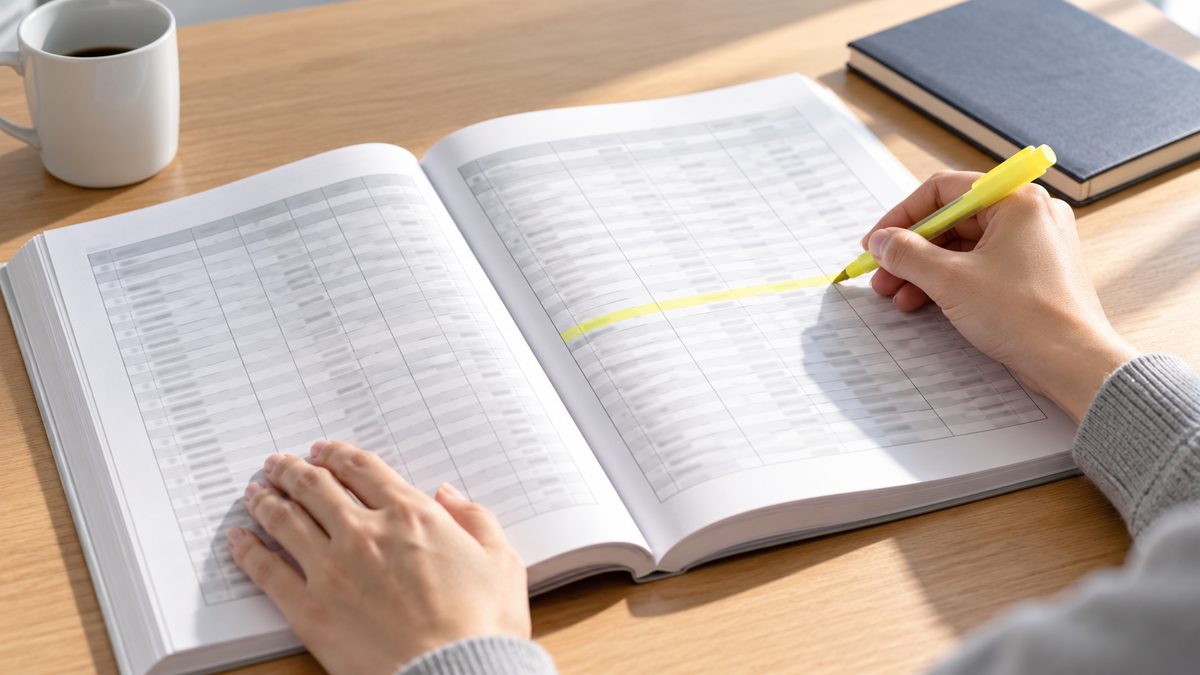 統計の冊子の表の1行に人事担当が蛍光ペンで線を引く手元